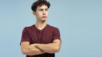 Serious, sad teen boy with crossed arms looking away on copy space, standing on blue background